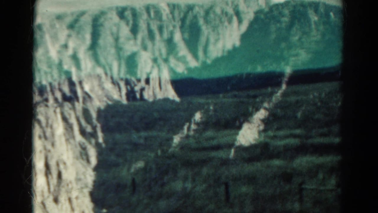 Rocky cliff and mountain valley with distant ridges and dark foreground.