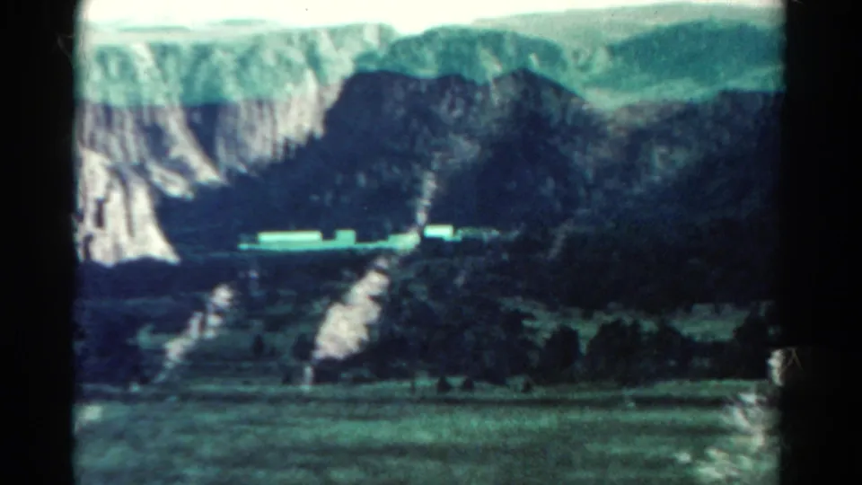 1967 Colorado 8mm view of cliffs, wooded valley terrain, and a light horizontal feature that may be a road or small structure.