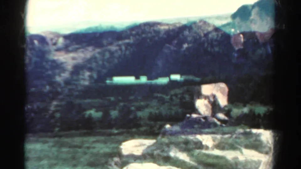 1967 8mm home-movie view of rugged Colorado terrain with distant mountains, scrub, and pale roadside forms.