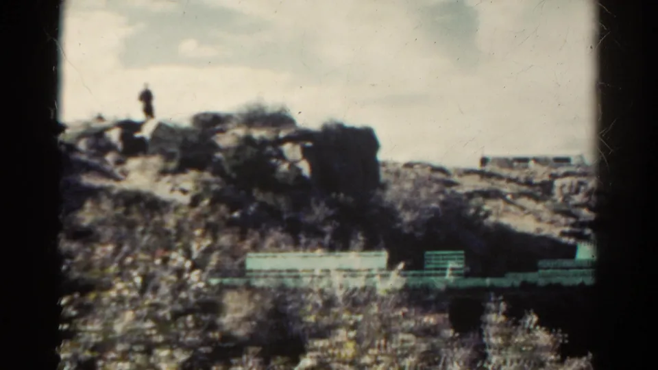 A distant person stands on rocky high ground while pale rail-like forms cross the lower Colorado landscape.