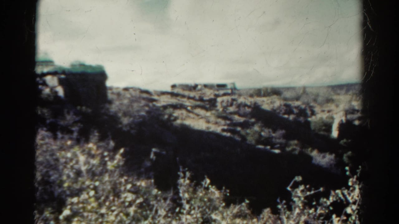 1967 Colorado 8mm frame showing a rugged canyon view, scrub plants, pale sky, and visible black gate edges.