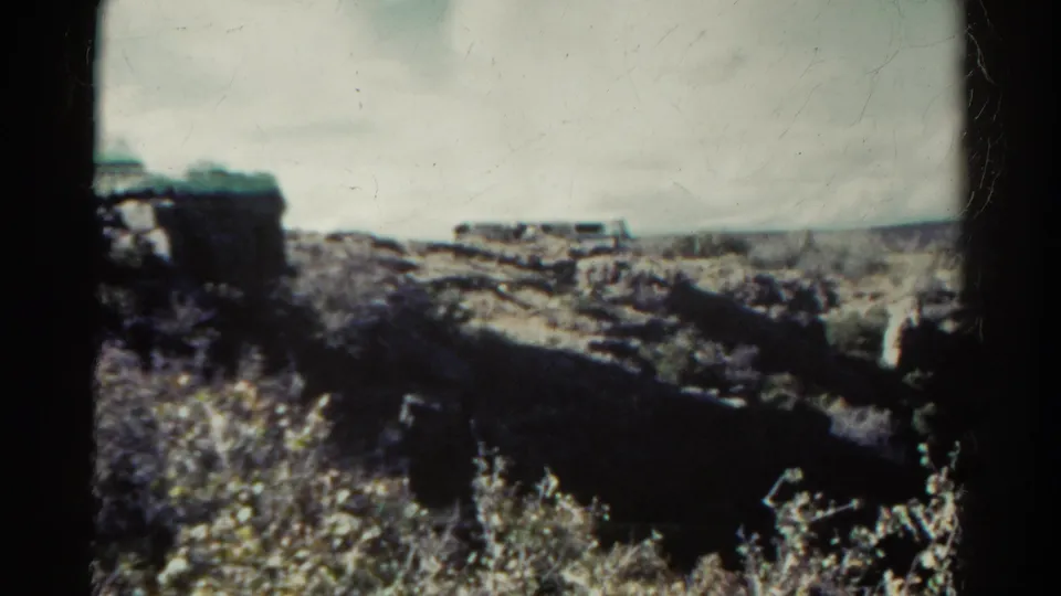 1967 Colorado 8mm frame showing a rugged canyon view, scrub plants, pale sky, and visible black gate edges.