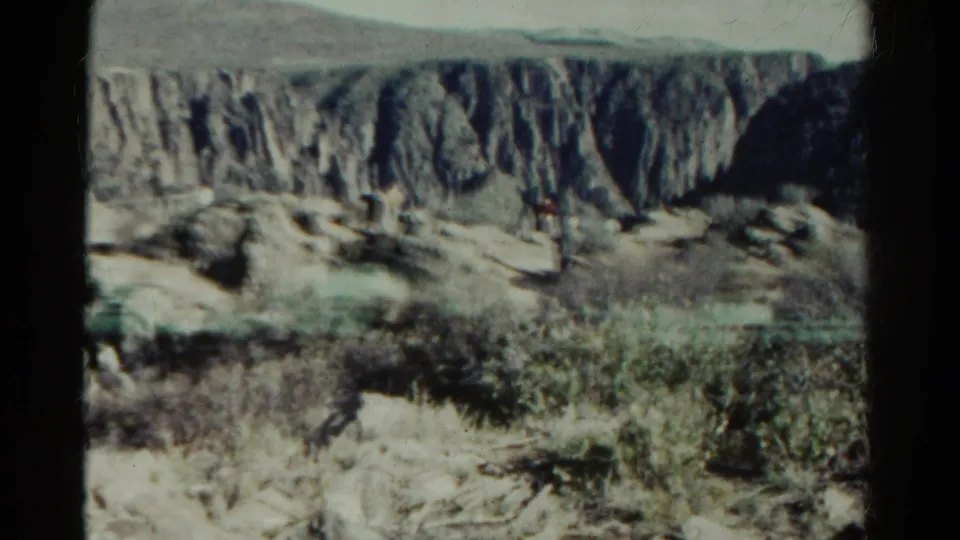 1967 Colorado 8mm frame showing a wider canyon wall with scrub vegetation, pale rock, and dark gate-edge shadow.