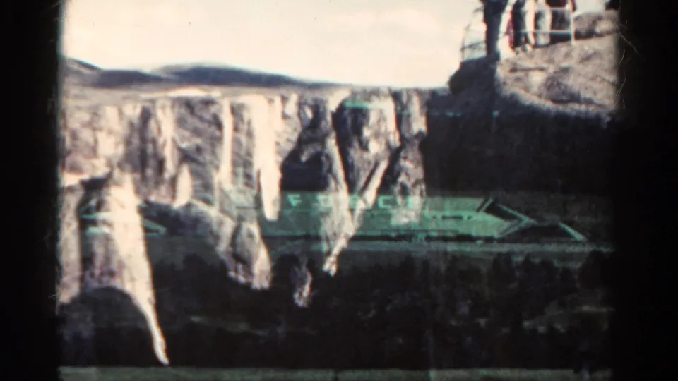 1967 Colorado 8mm frame showing a wider pass across pale cliffs, distant hills, and a partially visible Air Force stadium below.