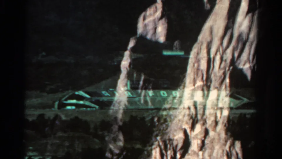 1967 Colorado 8mm frame where a dark rock wall obscures part of the Air Force stadium as the camera passes the landscape.