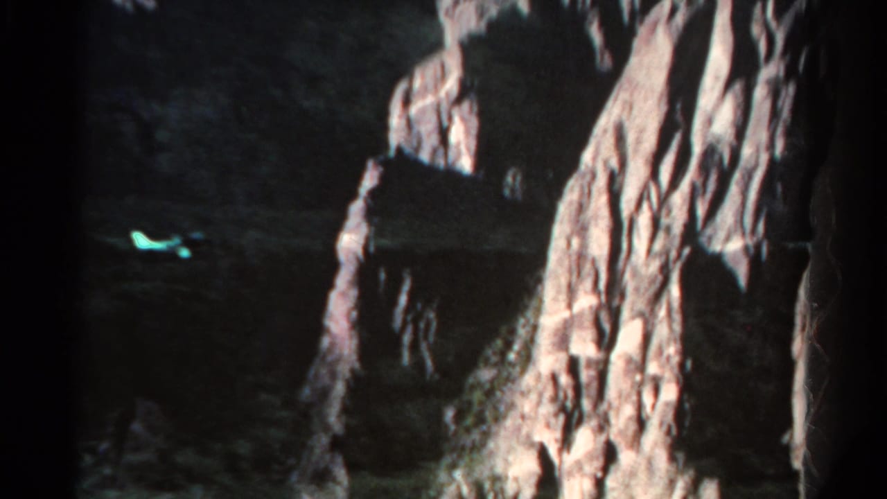 1967 Colorado 8mm frame showing a shadowed cave or cliff opening beside pale rock walls, with a small greenish reflection in the dark foreground.