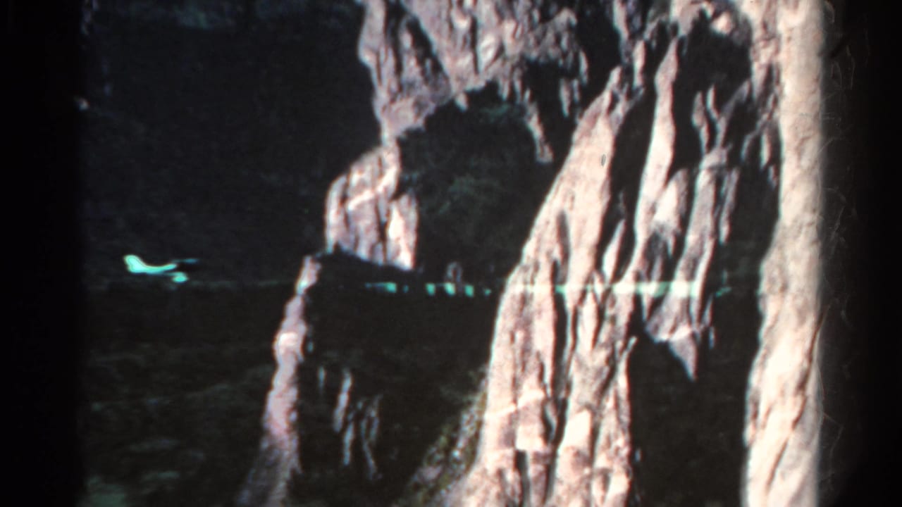 1967 Colorado 8mm frame with a dark cave-like opening, steep textured rock, and a small greenish reflection across the shadowed lower area.