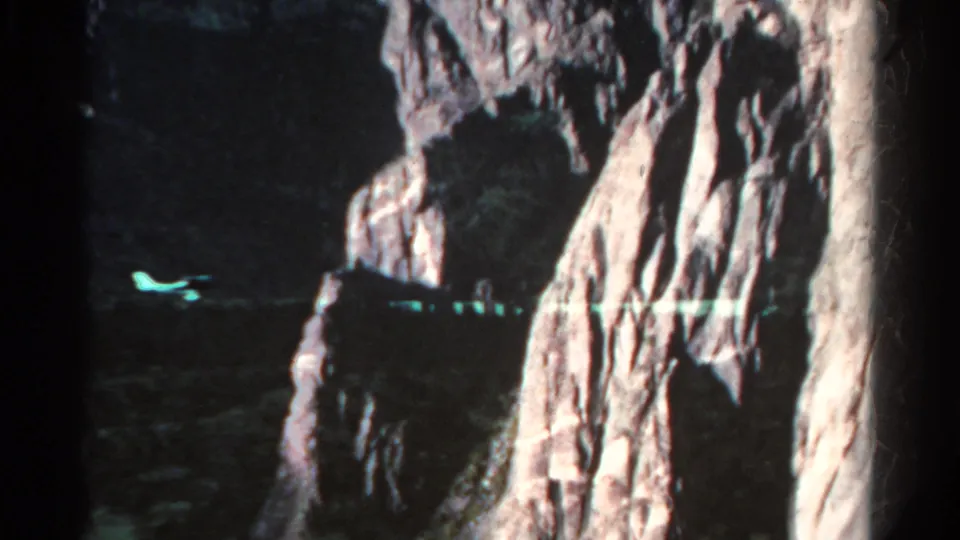 1967 Colorado 8mm frame with a dark cave-like opening, steep textured rock, and a small greenish reflection across the shadowed lower area.