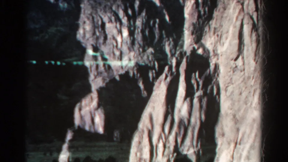1967 Colorado 8mm frame showing rough pale rock formations around a dark cave or recess, with greenish film streaking and shadow below.