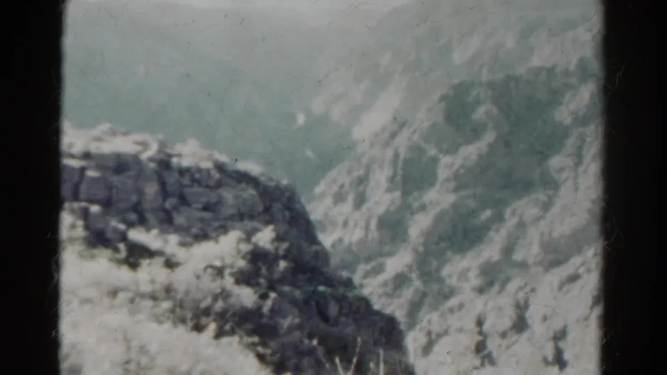 1967 8mm Colorado landscape showing a snowy rock ledge and distant mountain slopes under muted light.