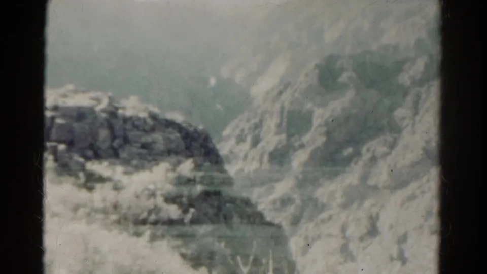 Faded 1967 8mm Colorado mountain frame with a snow-lined ridge, hazy slopes, and visible film wear.