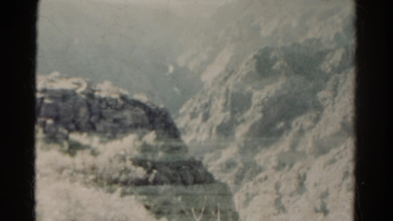 1967 Colorado 8mm frame showing a rocky slope and pale plains through soft grain, dust, and dark film-edge borders.