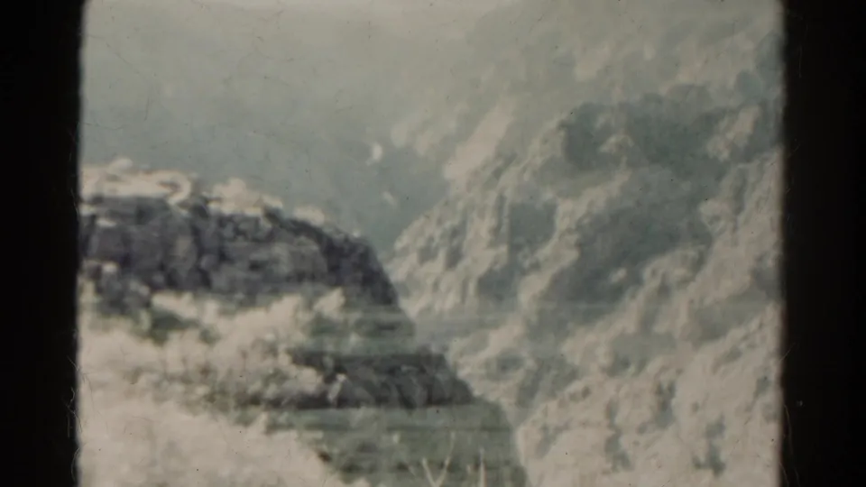 1967 Colorado 8mm frame showing a rocky slope and pale plains through soft grain, dust, and dark film-edge borders.