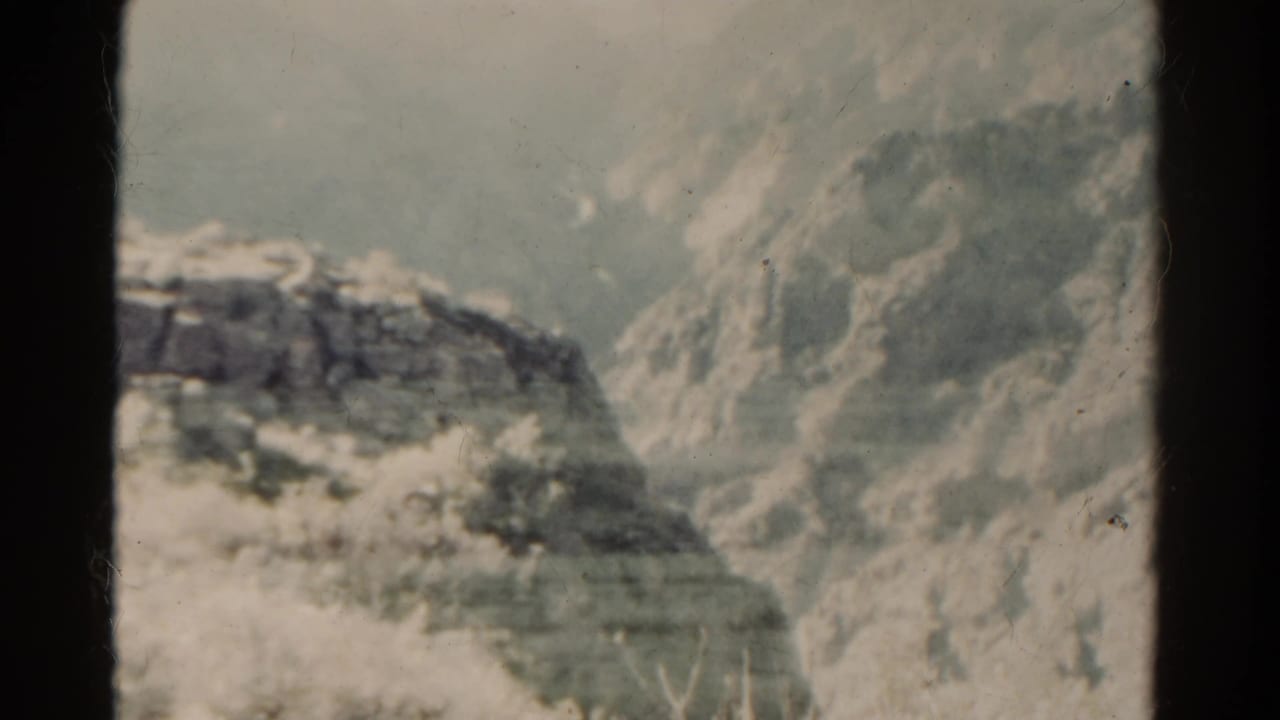 1967 Colorado home-movie frame with a rocky ridge, open plains, muted color, and visible 8mm film wear.