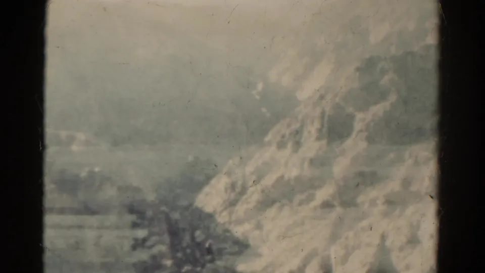1967 Colorado 8mm frame showing a pale rocky slope and broad plain with softened focus and surface marks from the film scan.