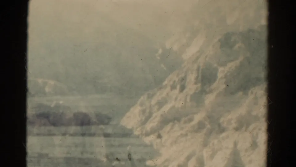 1967 Colorado 8mm frame showing a rocky slope beside a pale open landscape, viewed through dark window edges from a moving vehicle.