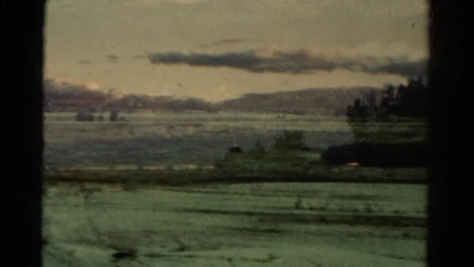 1967 Colorado landscape with broad fields, distant mountain ridges, scattered trees, and dark vehicle-window framing at the edge.