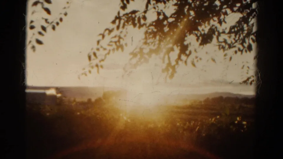 Colorado 1967 home-movie still with bright dusk glare, silhouetted foliage, and a soft rural horizon.