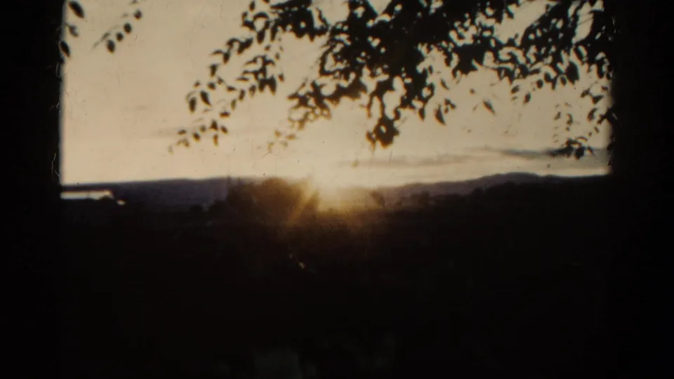 1967 Colorado 8mm frame showing the sun low behind a dark rural foreground with hills and branches visible.