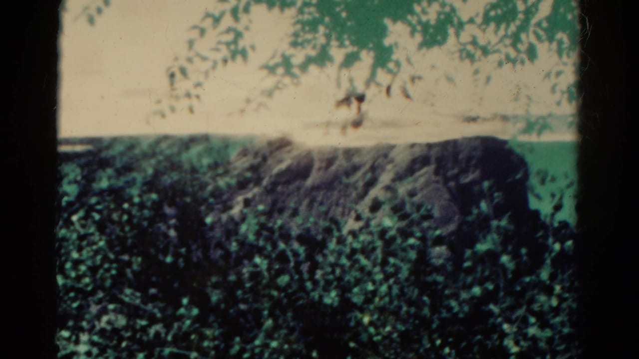 1967 Colorado 8mm frame showing a rocky cliff beyond trees, with blue-green sky and visible film-frame edges.