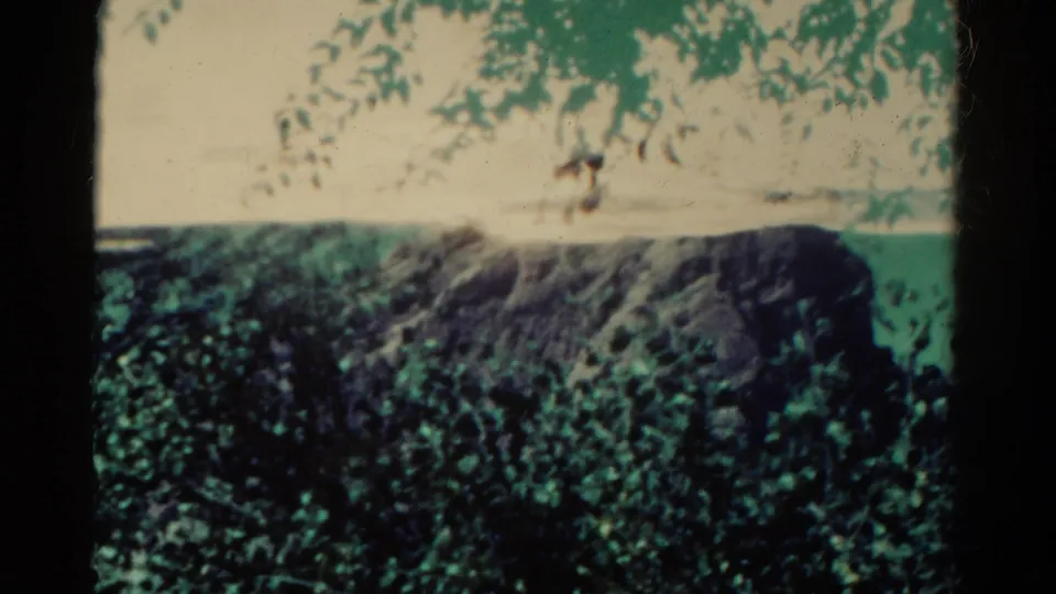 1967 Colorado 8mm frame showing a rocky cliff beyond trees, with blue-green sky and visible film-frame edges.