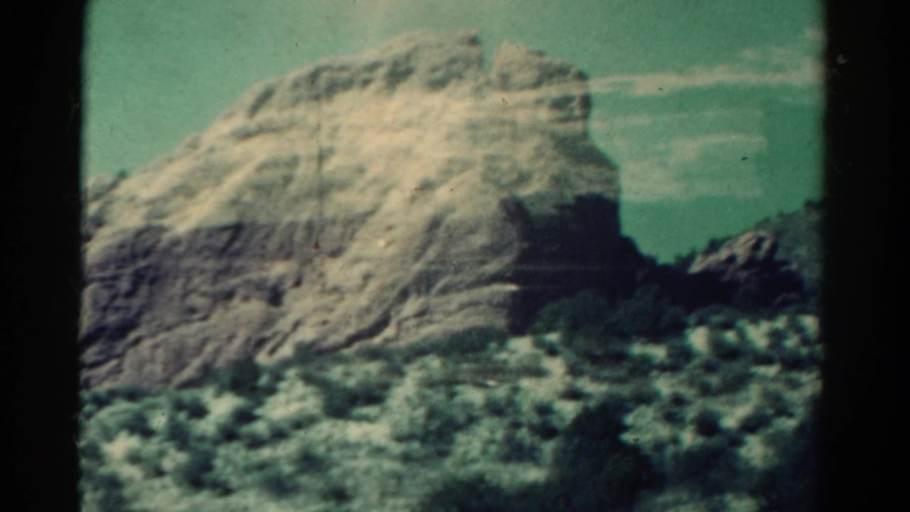 1967 Colorado 8mm frame showing a rugged rock formation, low vegetation, and faded green-blue sky.