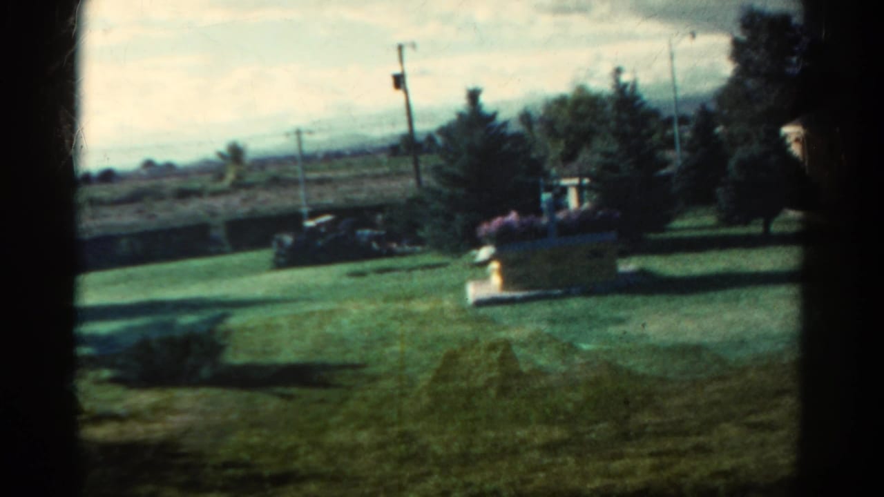 1967 Colorado suburban yard with a planter of flowers, trimmed lawn, parked car, trees, and utility poles in the distance.