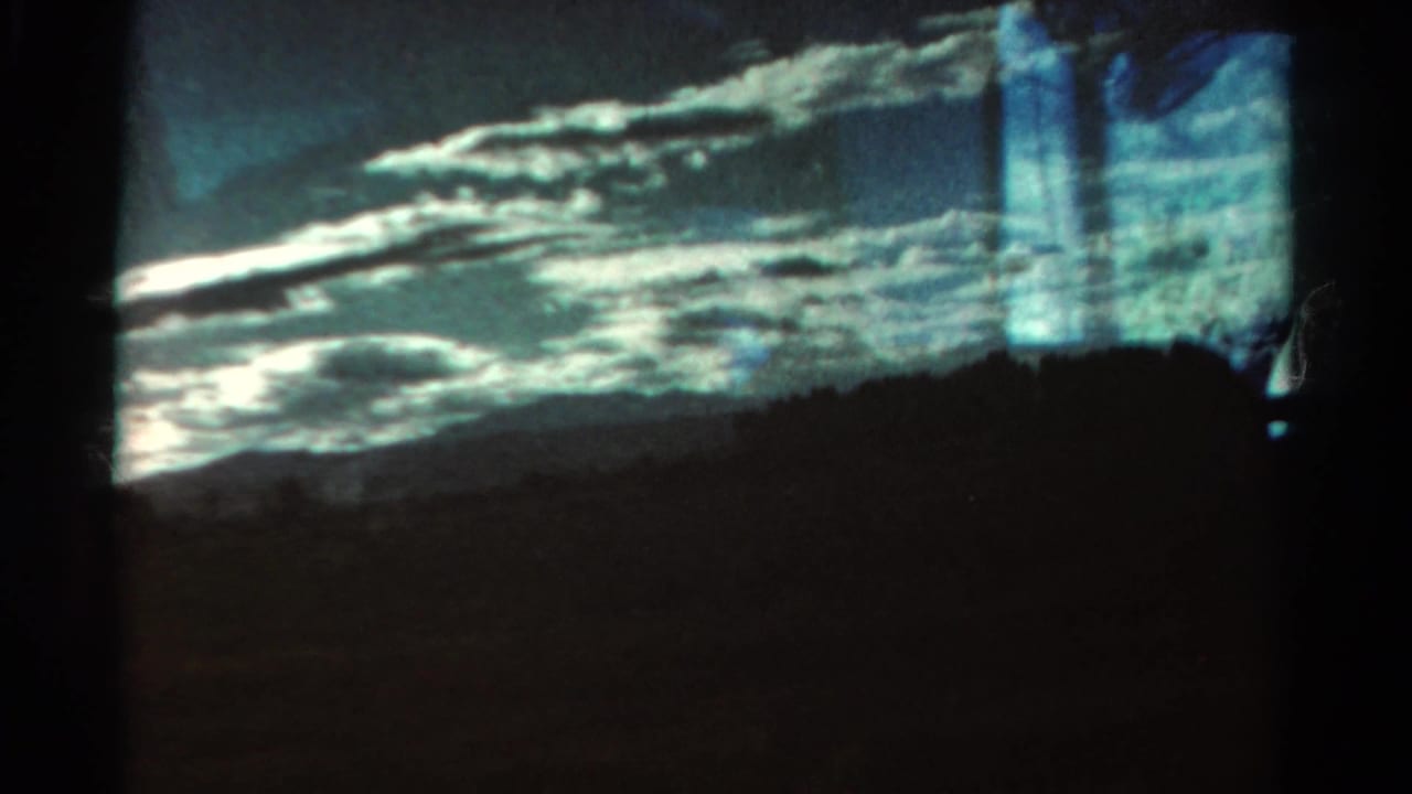 Cloudy mountain view with dark ridge line and window-like reflections at the frame edge.