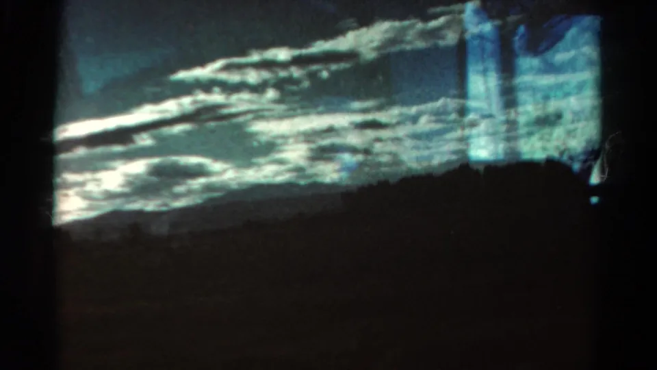 1967 Colorado 8mm frame with a dark mountain silhouette, bright horizontal clouds, blue-green cast, and faint vertical reflections near the right edge.