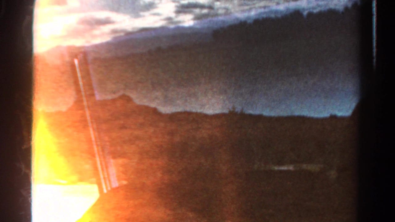 1967 Colorado home-movie frame showing a dark rural roadside view from a moving car, with distant hills and strong orange light leak.