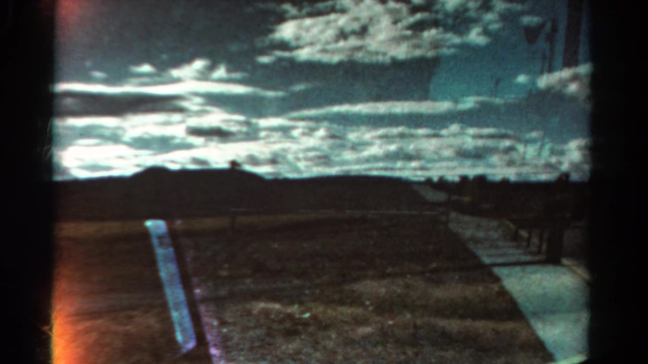 Cloud-filled sky above a rural roadside with fence posts and a pale strip at the right.