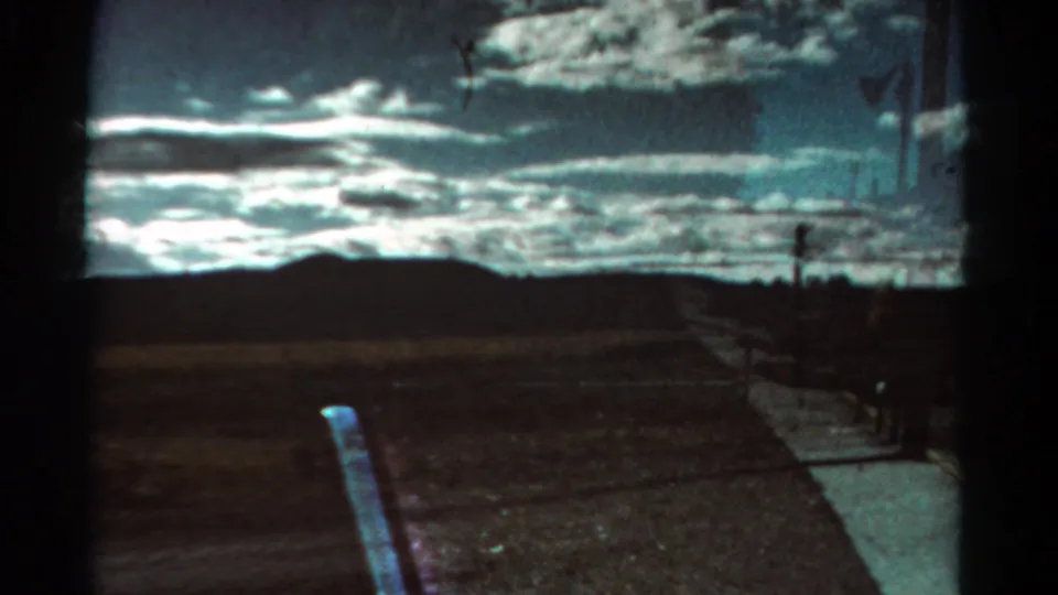 Colorado 1967 car-window footage frames open roadside land, distant low hills, fence posts, and a bright cloud band across the sky.