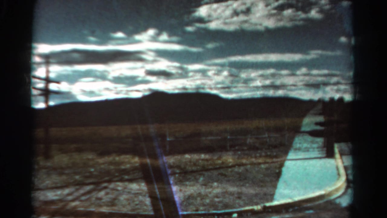 1967 Colorado 8mm frame showing dry open terrain, distant low mountains, fence line, utility pole, and bright clouds.