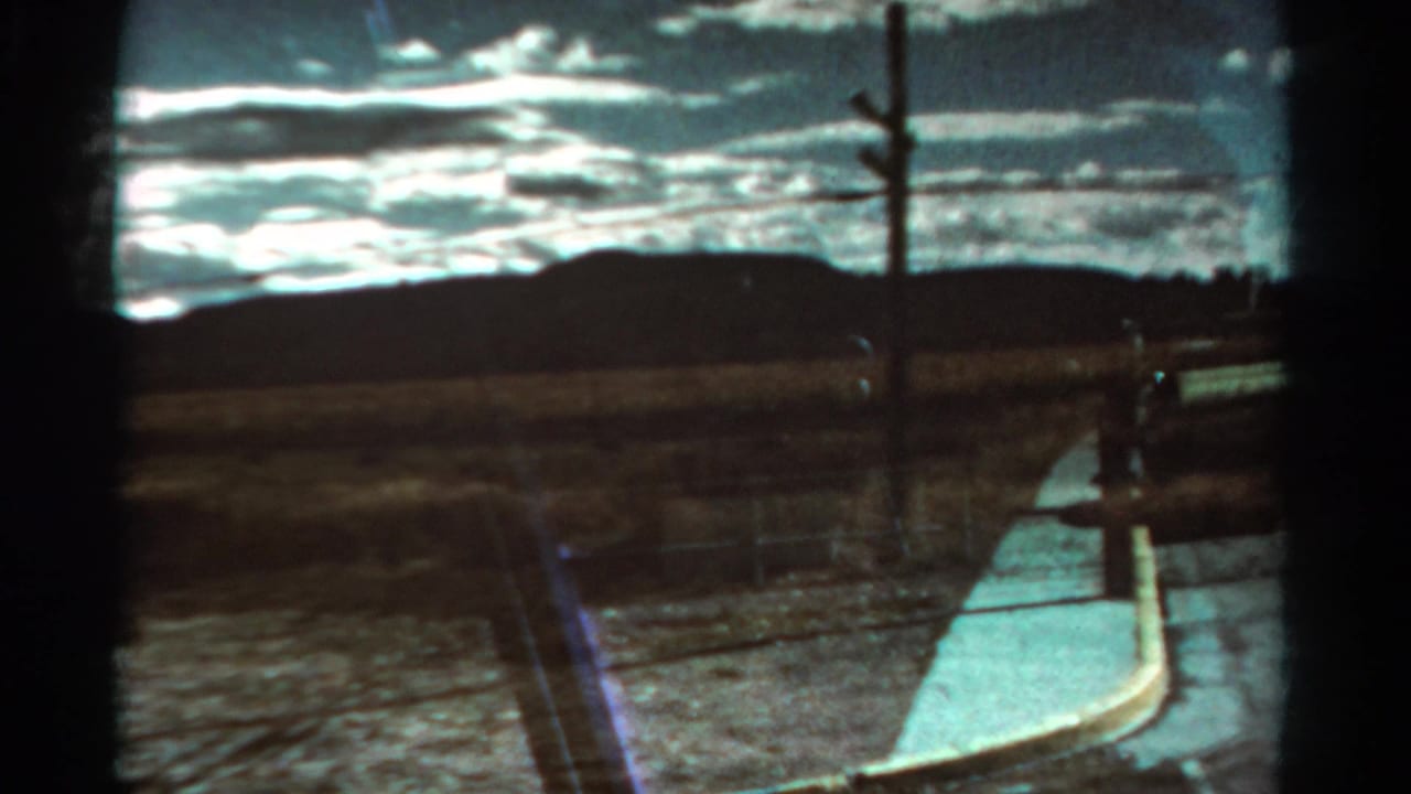 Roadside path, fence, utility pole, open dry land, and distant mountain ridge.