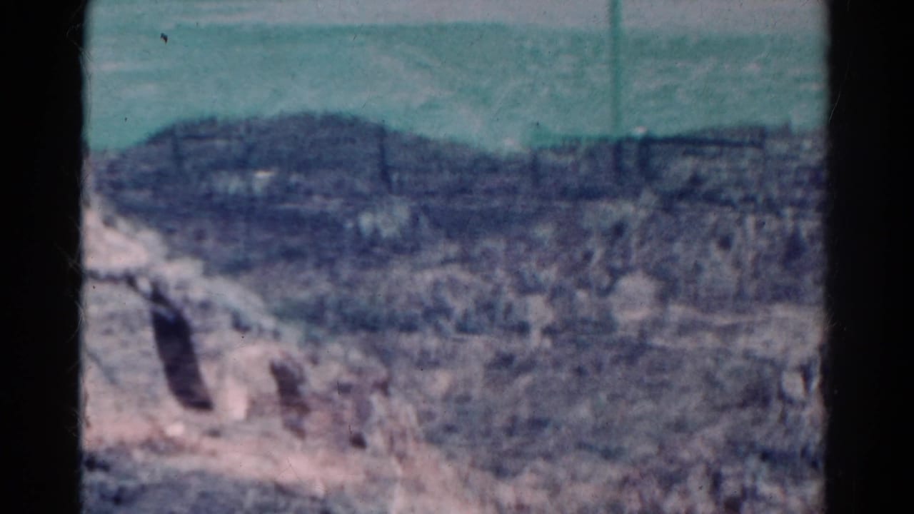 1967 Colorado 8mm frame showing a high-angle view over rocky, scrub-covered terrain beneath a pale sky.