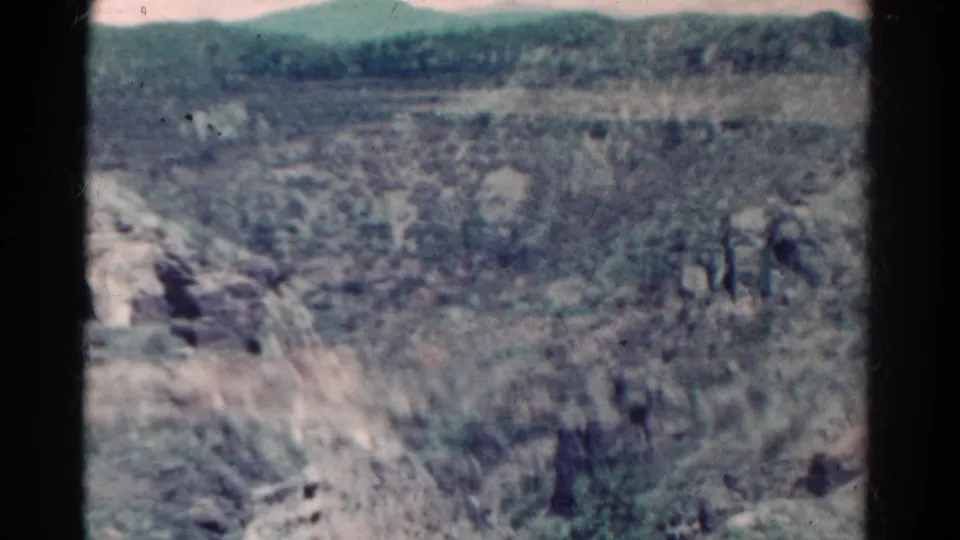 1967 Colorado home-movie frame showing rocky scrubland, uneven terrain, and low hills in faded color.