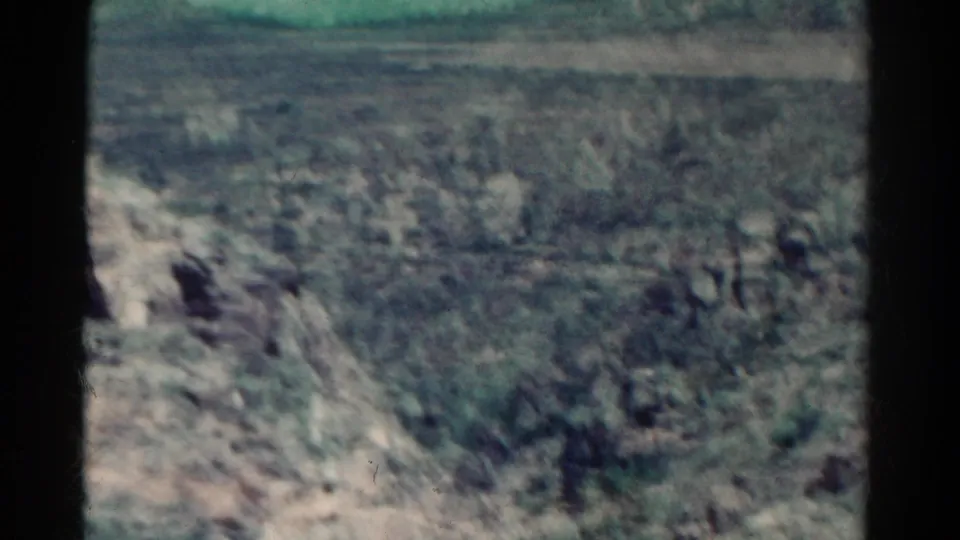 1967 Colorado 8mm frame showing a soft-focus rocky landscape with sparse brush and distant ridgeline.