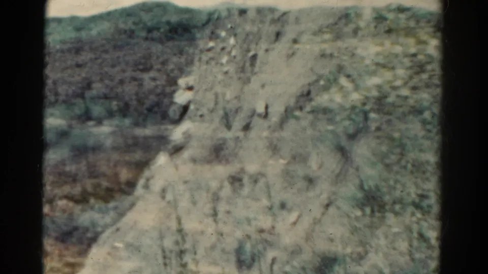 1967 Colorado 8mm frame showing a pale rocky canyon wall, scrub vegetation, and distant hills in faded color.