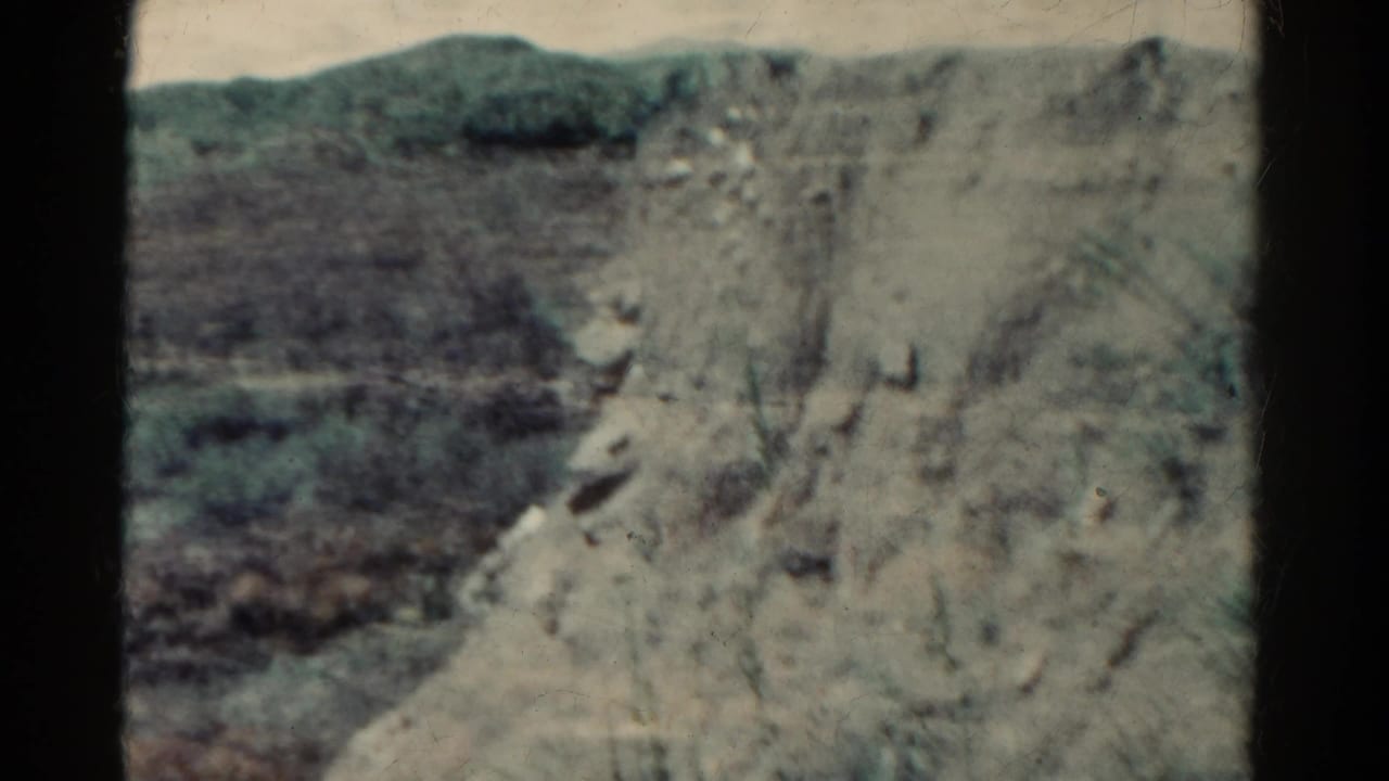 Rocky cliff face and distant hillside seen through dark film gate edges.