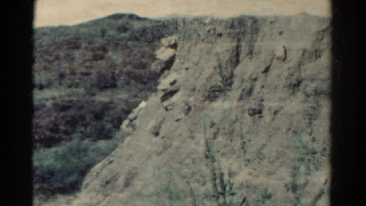 Steep pale rock slope with darker hills behind it.