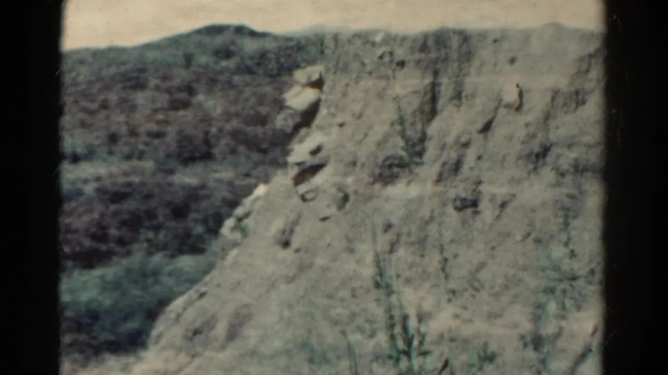 Colorado canyon terrain in 1967 home-movie footage, with a steep eroded rock face and shadowed hills beyond.