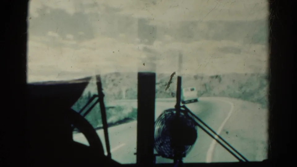 From inside the vehicle, the 1967 Colorado road bends ahead while a small fan and wiper arms silhouette against the dusty windshield.
