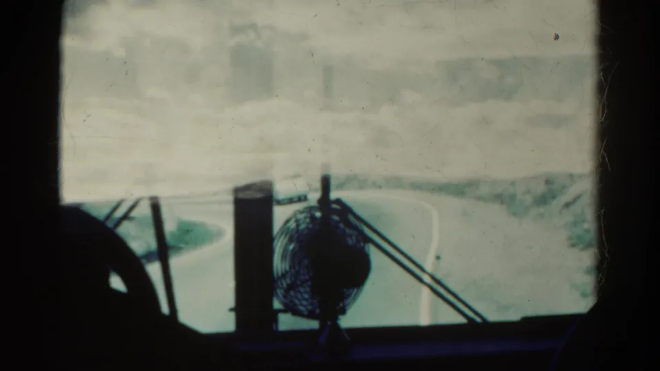Soft 8mm frame showing a Colorado road seen through a dirty vehicle windshield, with the dashboard fan prominent in the foreground.