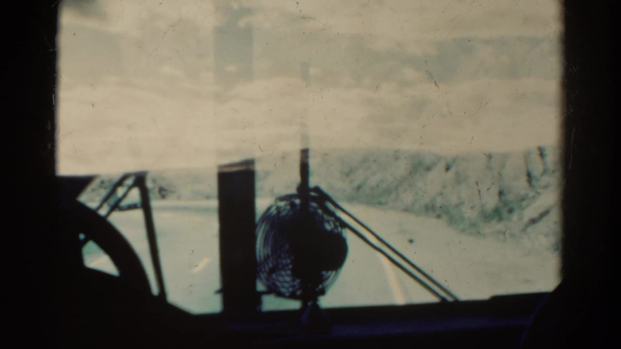 1967 Colorado 8mm frame from inside a vehicle, showing a dashboard fan and winding mountain road through the windshield.