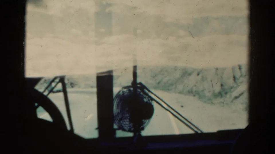 1967 Colorado 8mm frame from inside a vehicle, showing a dashboard fan and winding mountain road through the windshield.