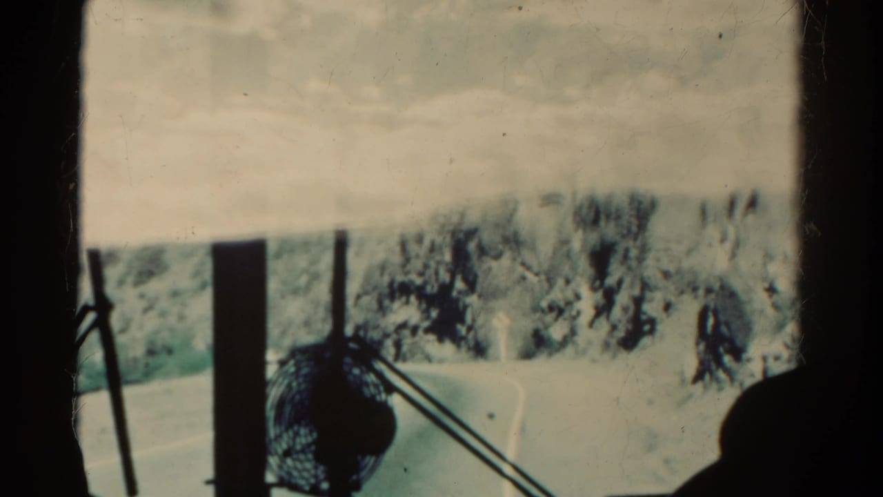 Windshield view past a dashboard fan toward a curving mountain road and rocky slope.