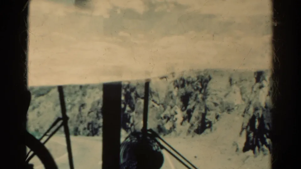 1967 Colorado vehicle POV showing the fan on the dash, windshield framing, and a narrow road running through rocky terrain.