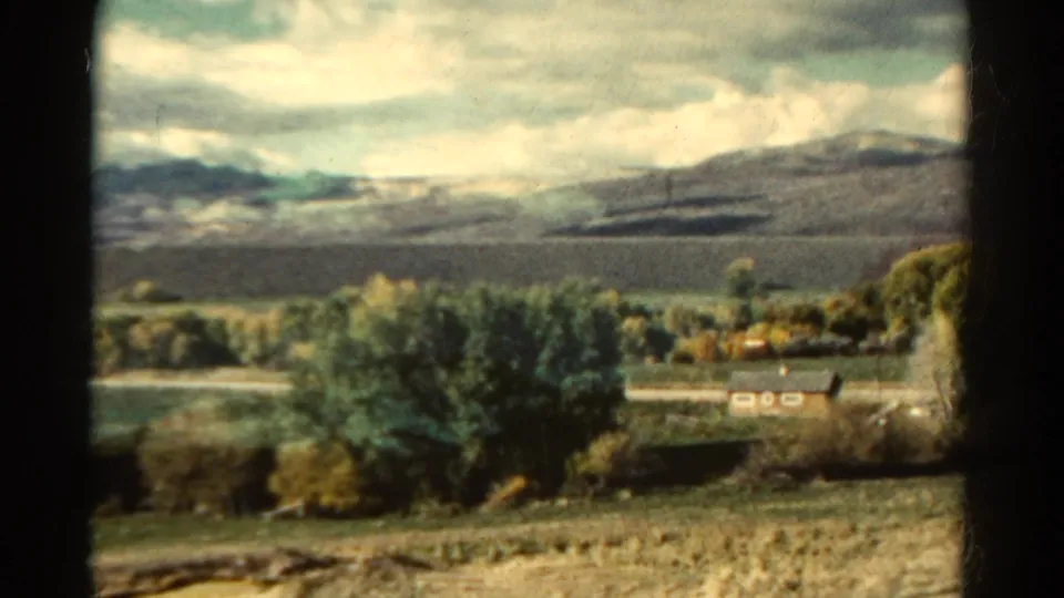 The final frame holds on Colorado countryside, with a house line, trees, open fields, mountains, and cloudy sky in soft 8mm color.