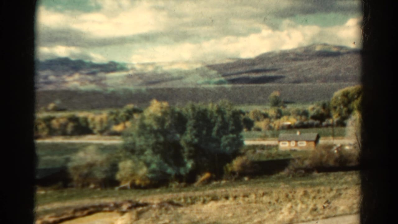Rural valley with trees, fields and distant mountains seen through dark frame edges.