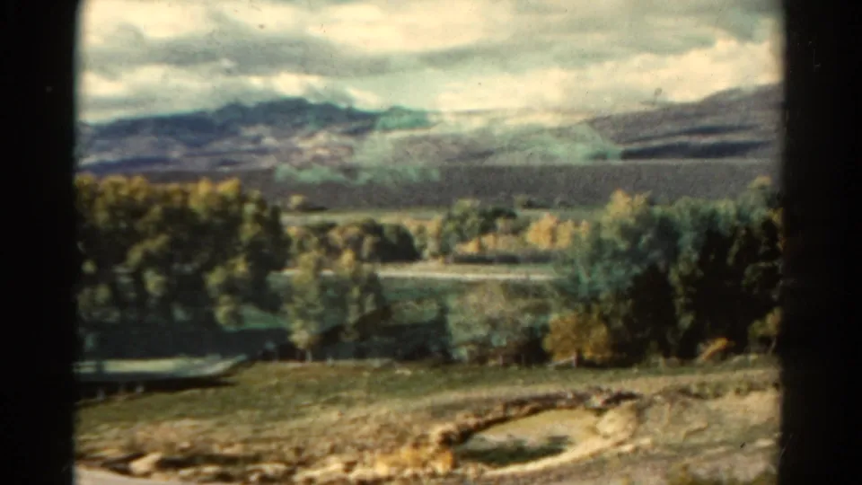 Soft 8mm frame of a Colorado rural valley in 1967, with open land, autumn trees and mountains in the distance.